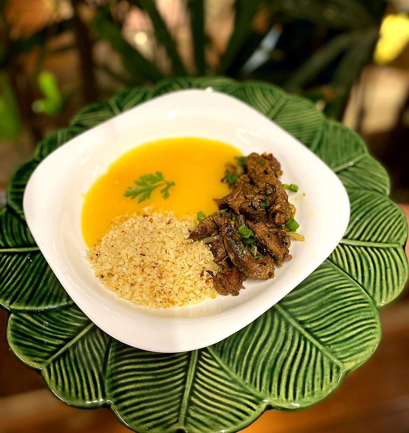 Filé mignon com purê de raízes e farofinha crocante, servido em prato branco sobre travessa em formato de folha